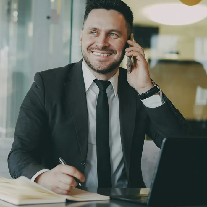 Een lachende man in pak aan de telefoon achter zijn bureau