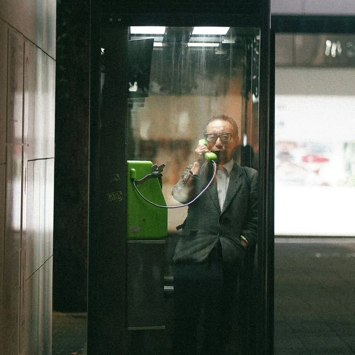 Een man in pak aan de telefoon in een glazen telefooncel
