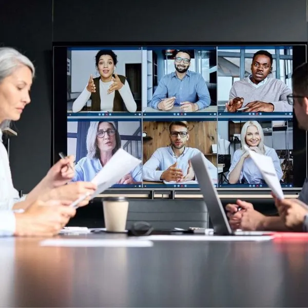 Een scherm in een vergaderruimte met een videogesprek met acht mensen