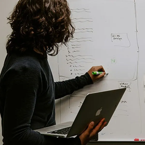 Een vrouw met een laptop in haar hand schrijft aantekeningen op een whiteboard
