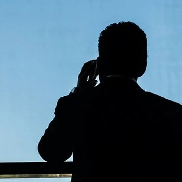 Het silhouet van een man aan de telefoon tegen een blauwe lucht