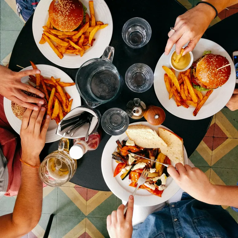 Mensen die hamburgers, friet en geroosterde groenten eten aan een ronde tafel, van bovenaf gezien