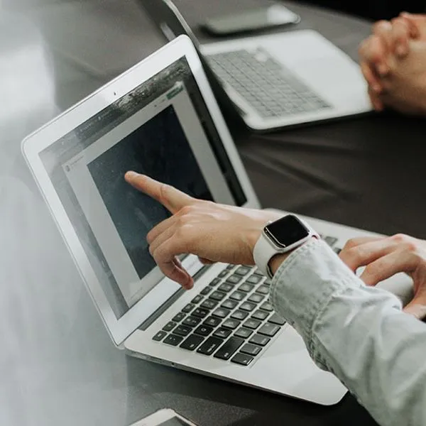 Twee mensen aan een tafel, van wie er één naar een laptopscherm wijst